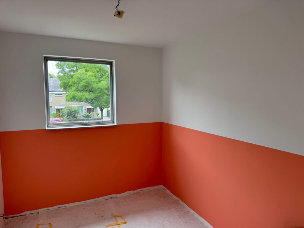 Kamer met oranje en witte muren en een raam.